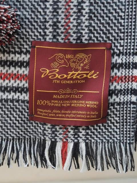 Bottoli label on a scarf showcasing 100% pure new merino wool, made in Italy, 5th generation craftsmanship.