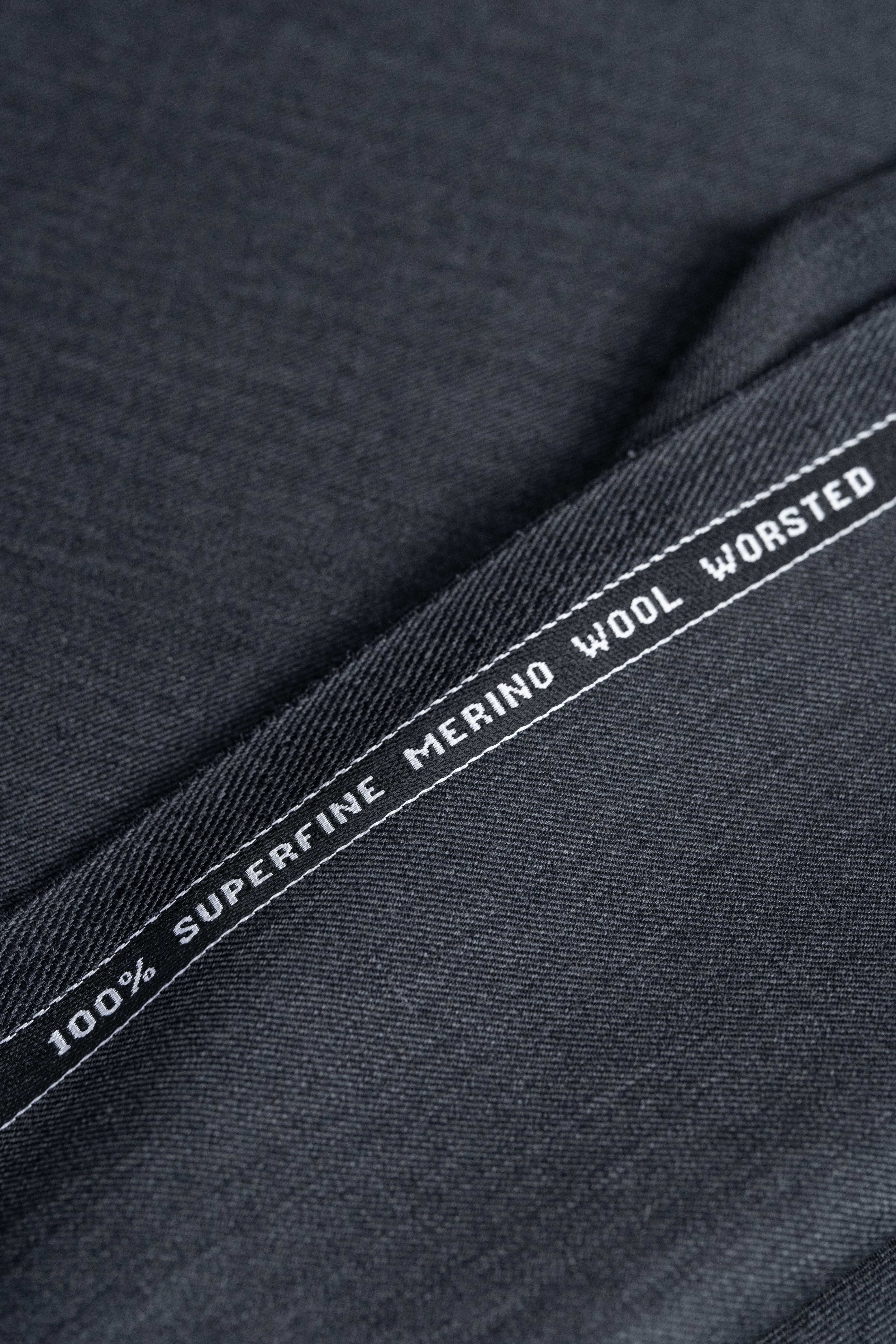 dark grey Super 100s wool suiting fabric with a label indicating 100% superfine merino wool worsted