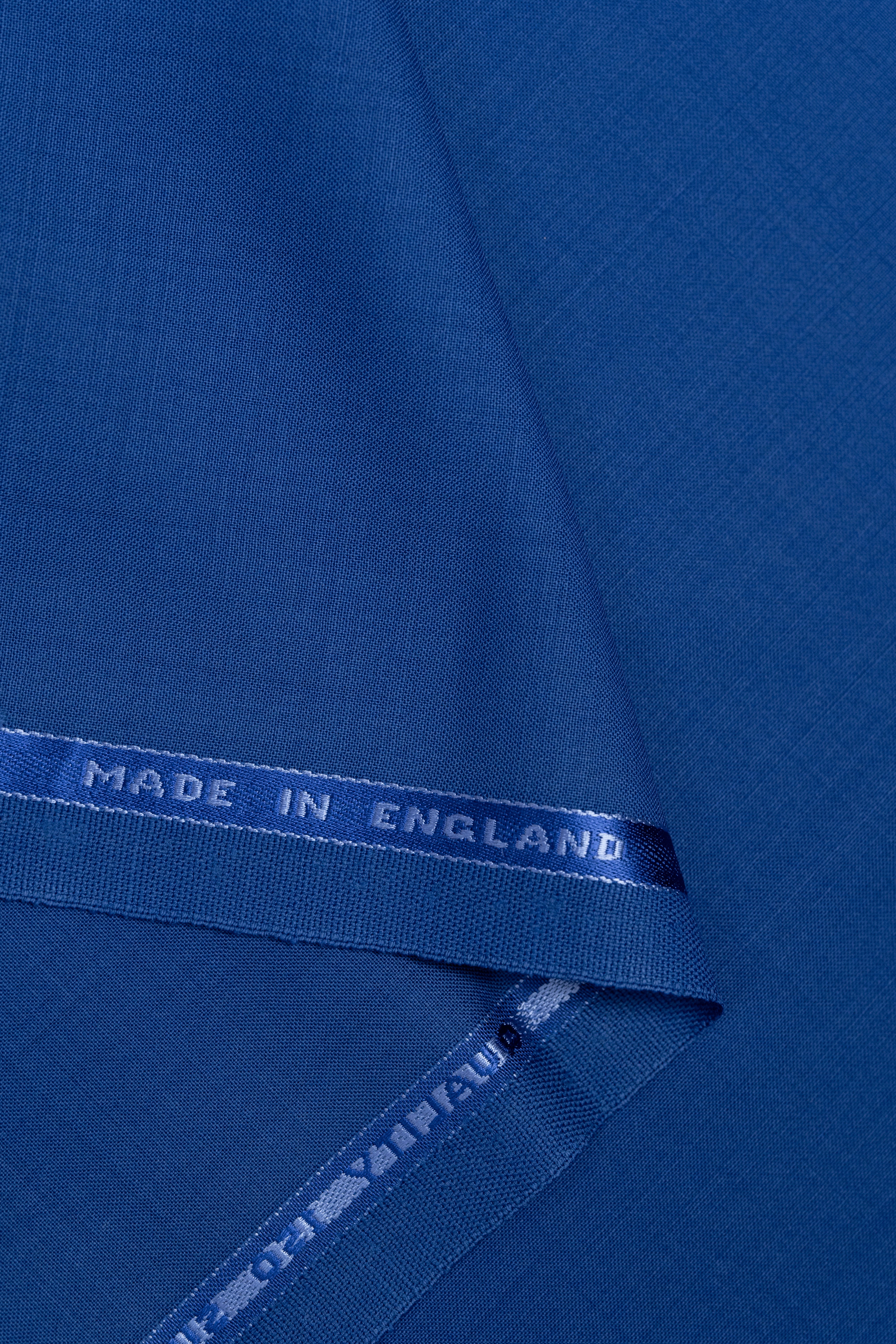 A close-up of folded royal blue fabric with a branded selvage edge reading 'MADE IN ENGLAND' and 'OFF VILLEUS' visible along the selvage.