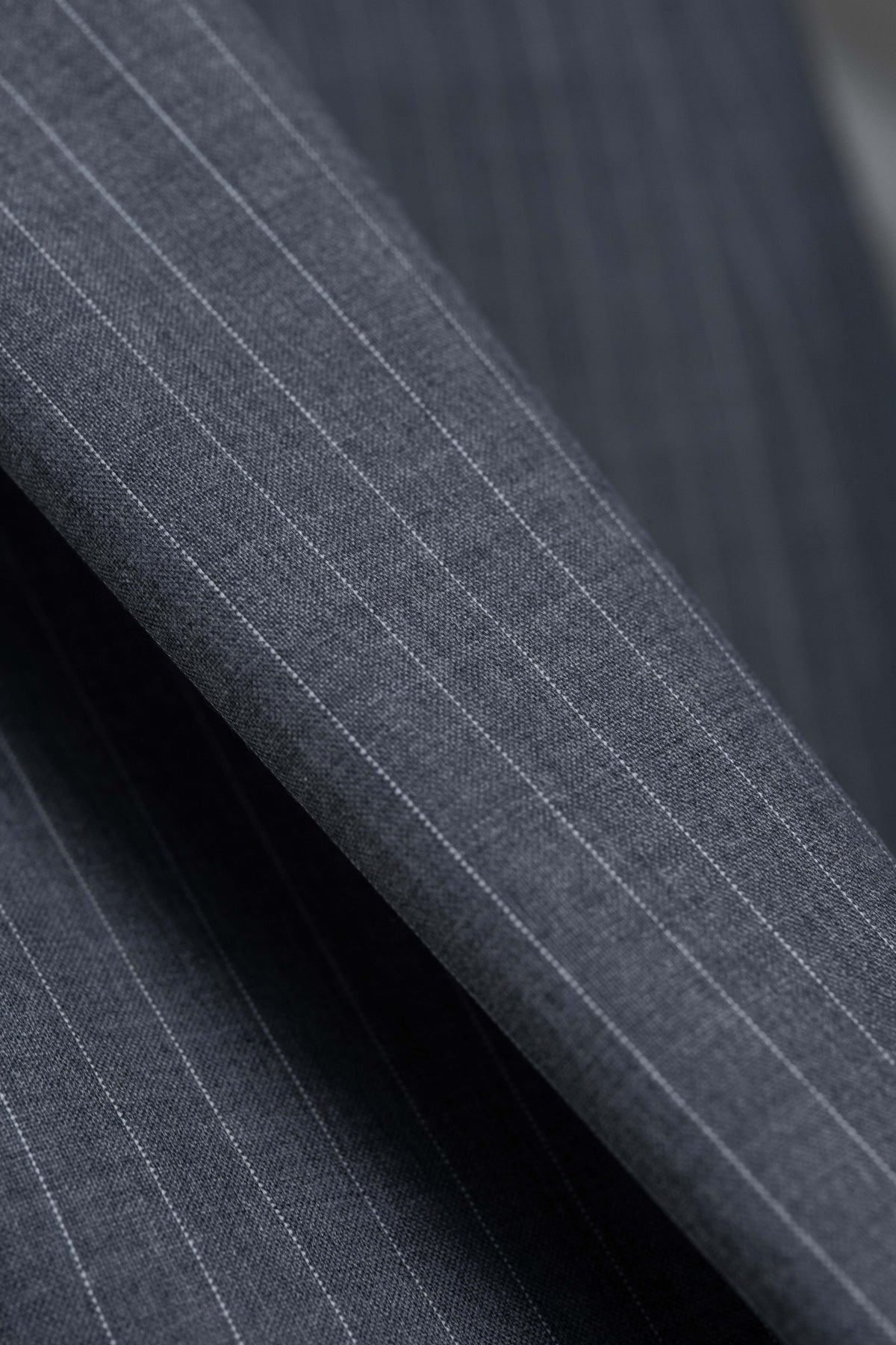 Close-up of grey stripe wool suiting fabric, showcasing the durable texture and classic pattern for trousers.