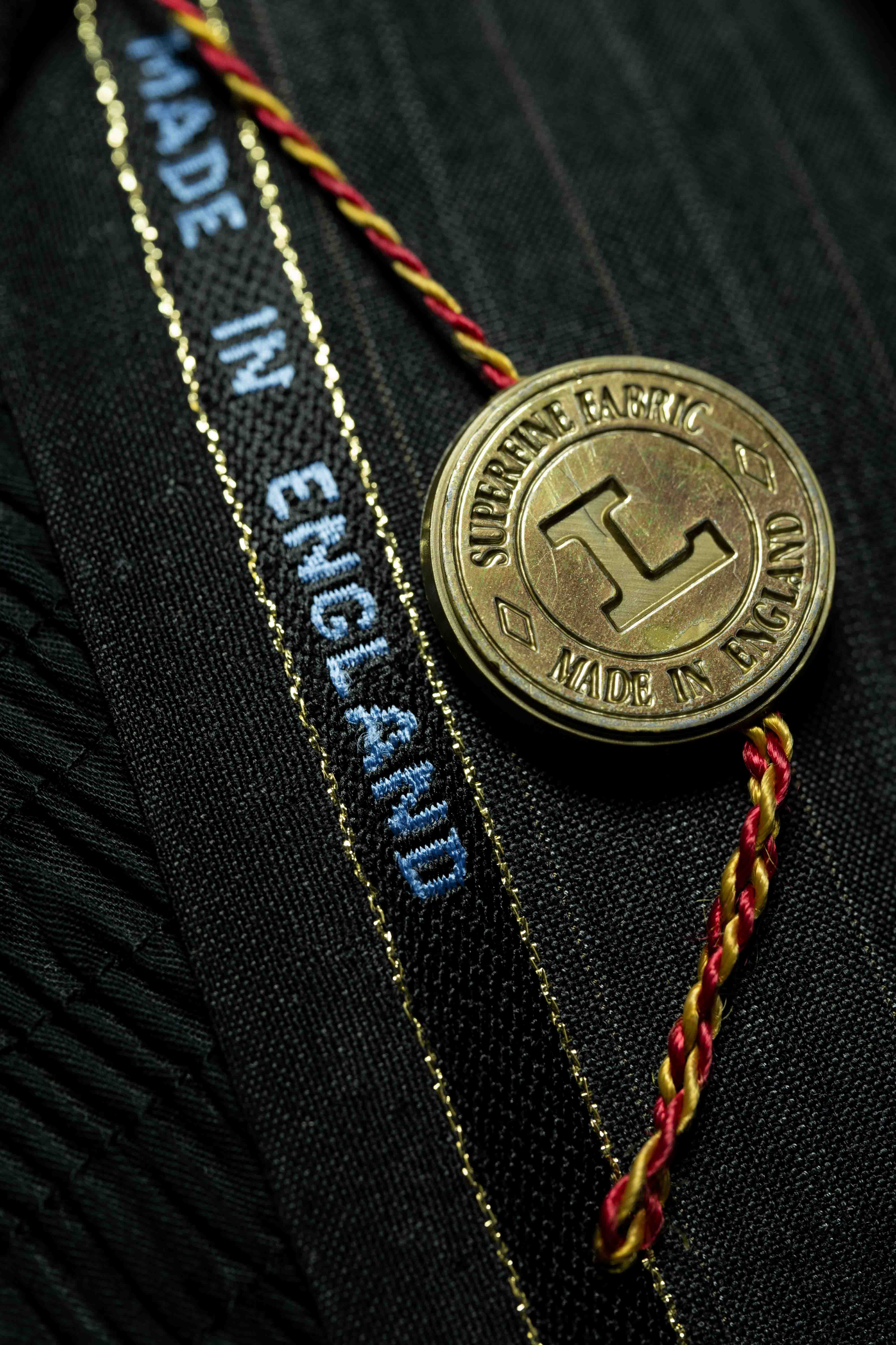 Lassitex charcoal stripe merino wool suit fabric label made in England and a gold coin badge.