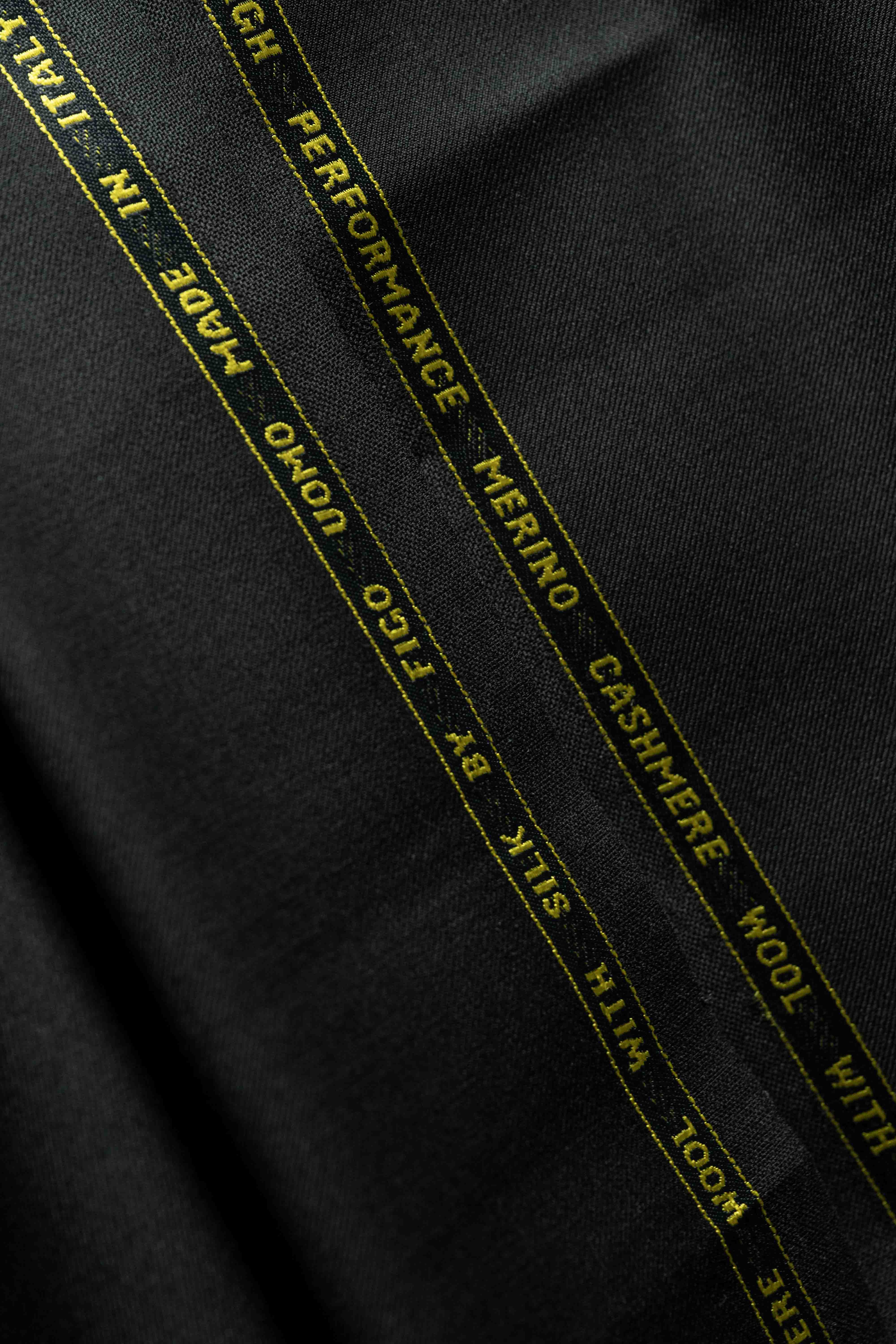 Black fabric featuring labels for Cashmere, Merino wool, and performance attributes for suit jacket construction.