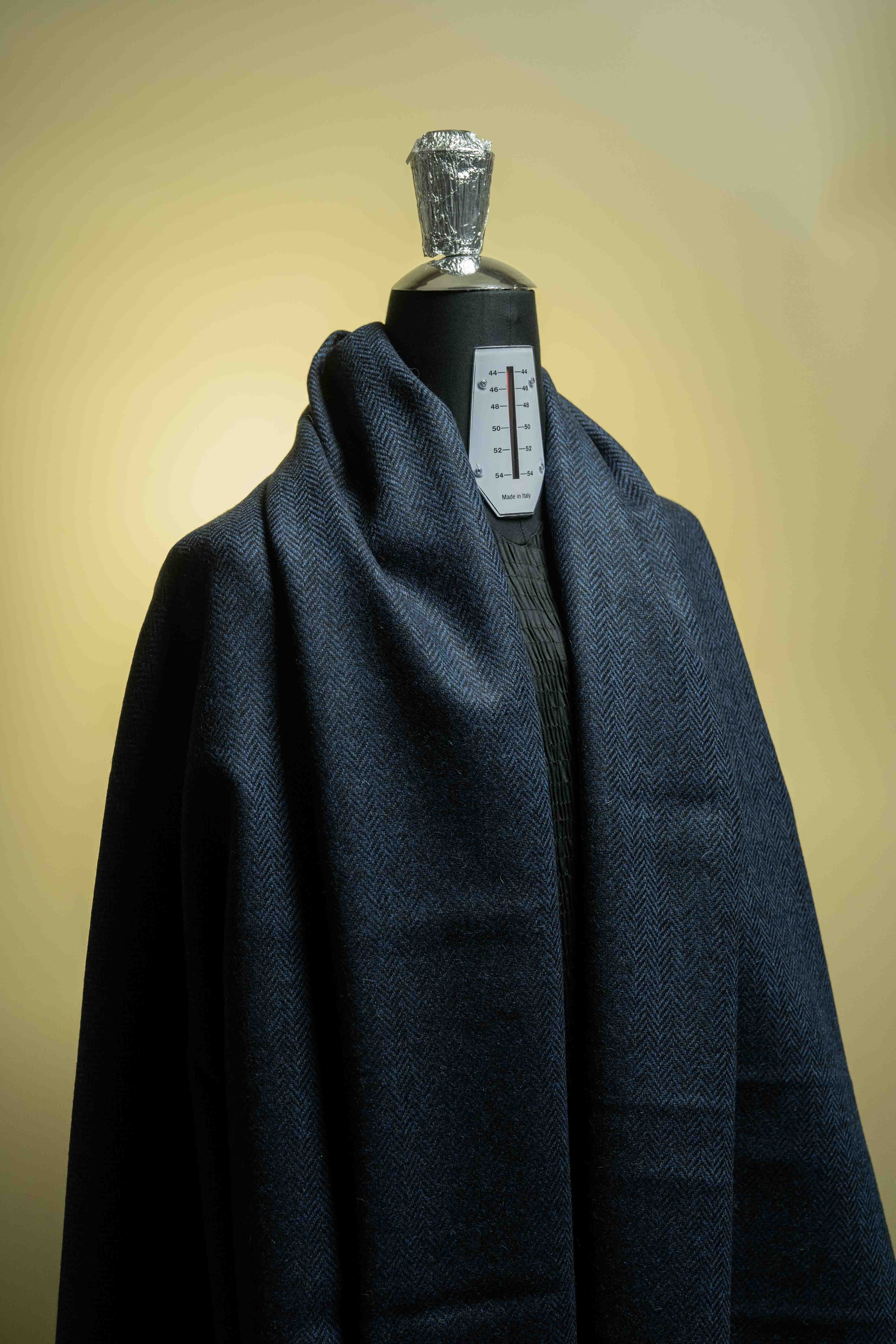Navy herringbone wool suit jacket fabric draped on a mannequin, showcasing high-quality suit fabric texture.