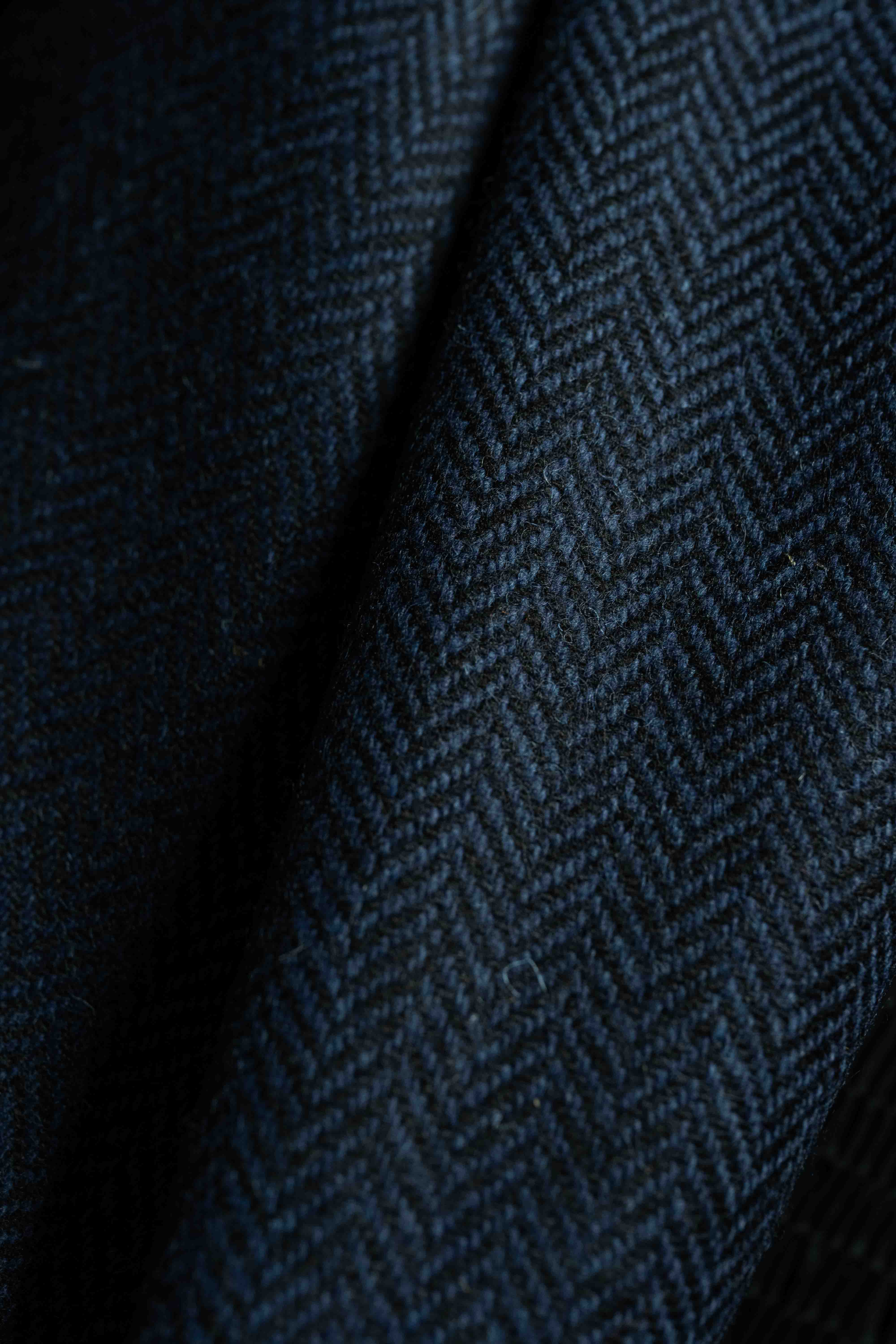 Close-up of navy herringbone wool suit fabric showcasing texture and pattern.