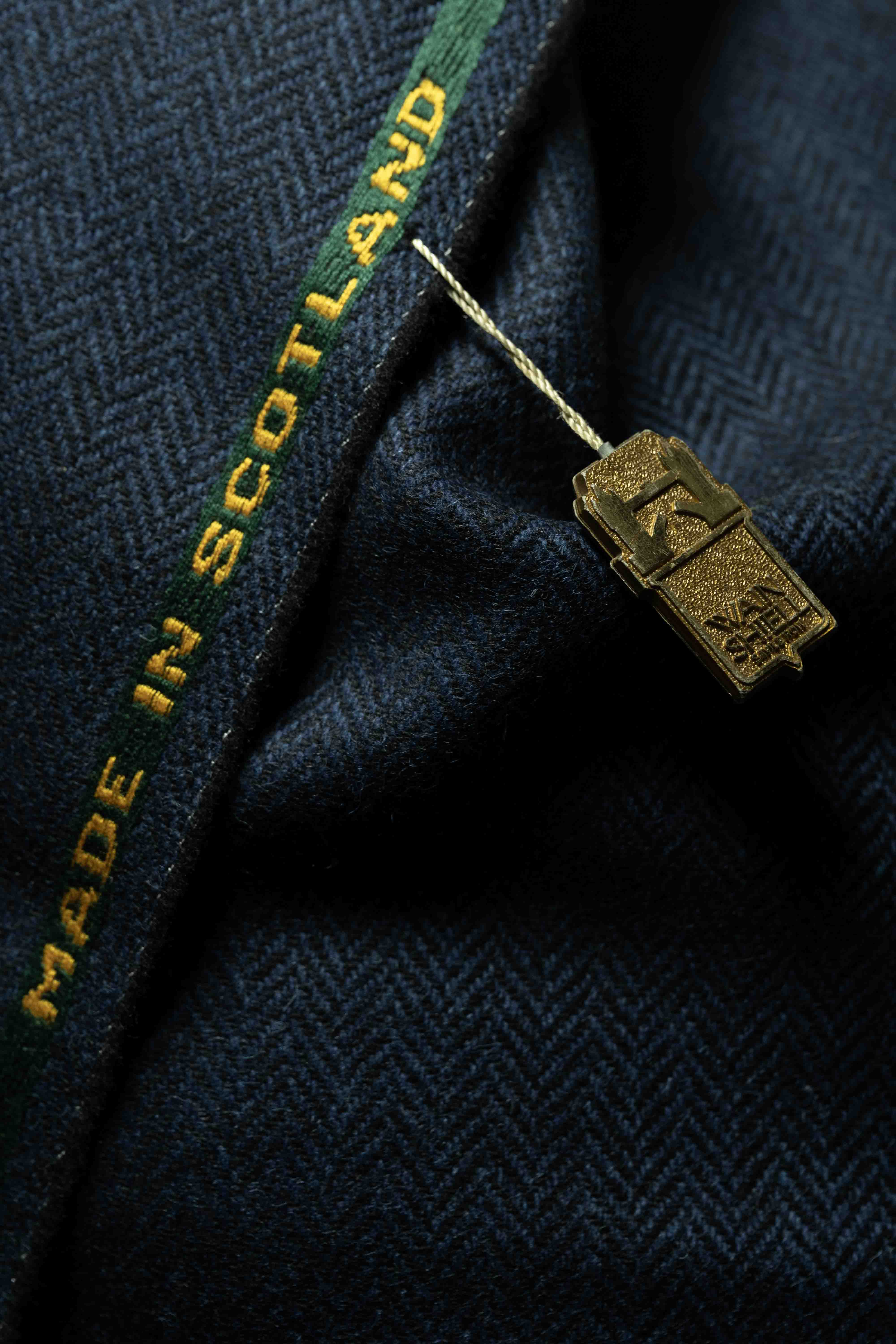 Detail of Navy Herringbone Wool Suit Jacket showcasing high-quality suit fabric and 'Made in Scotland' tag.